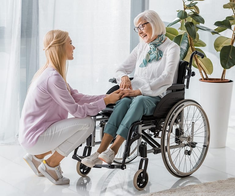 young woman speaking with senior woman in wheelchair at nursing home